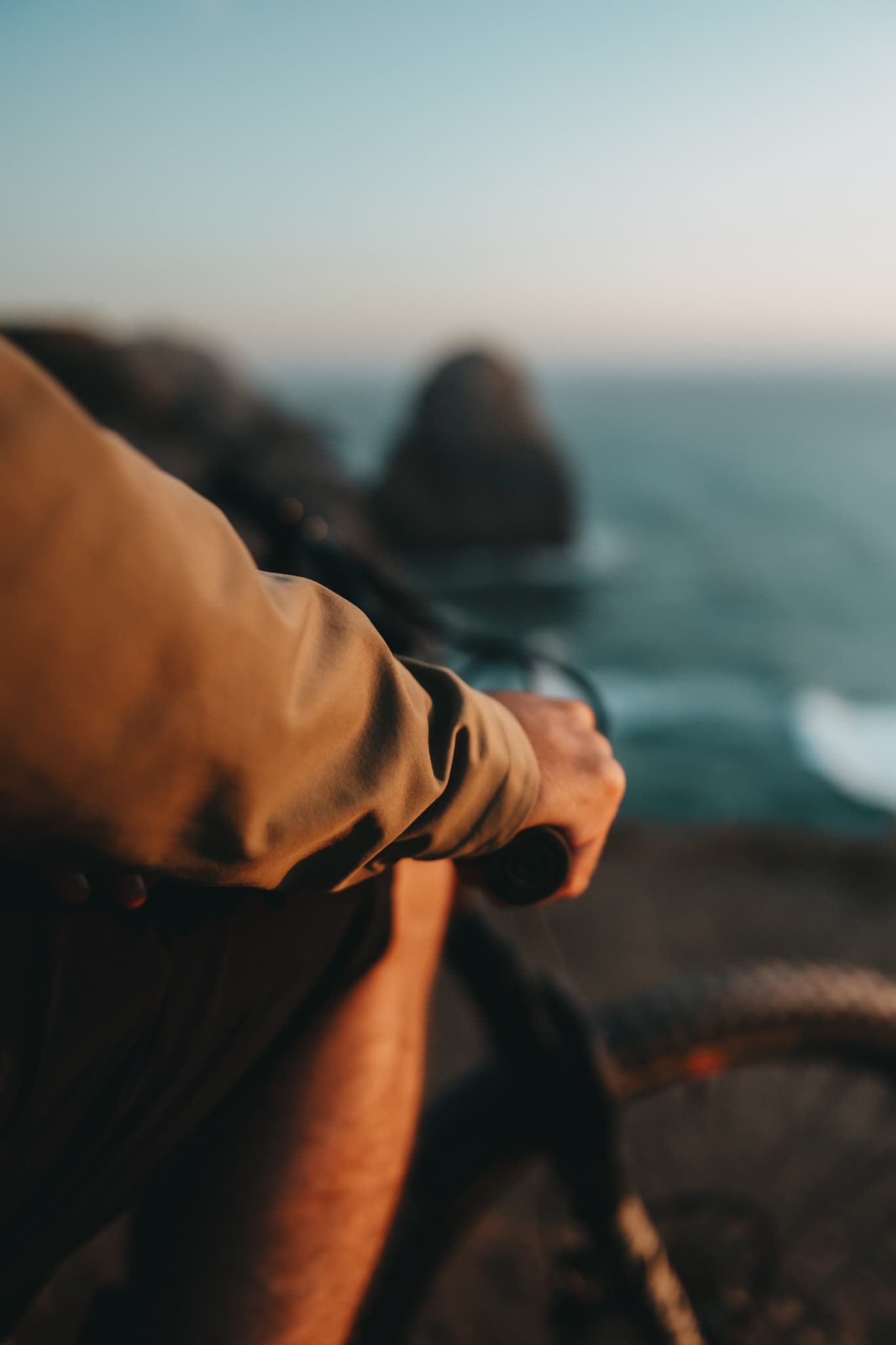 A hand resting on the handlebar above the Sintra coastline at golden hour