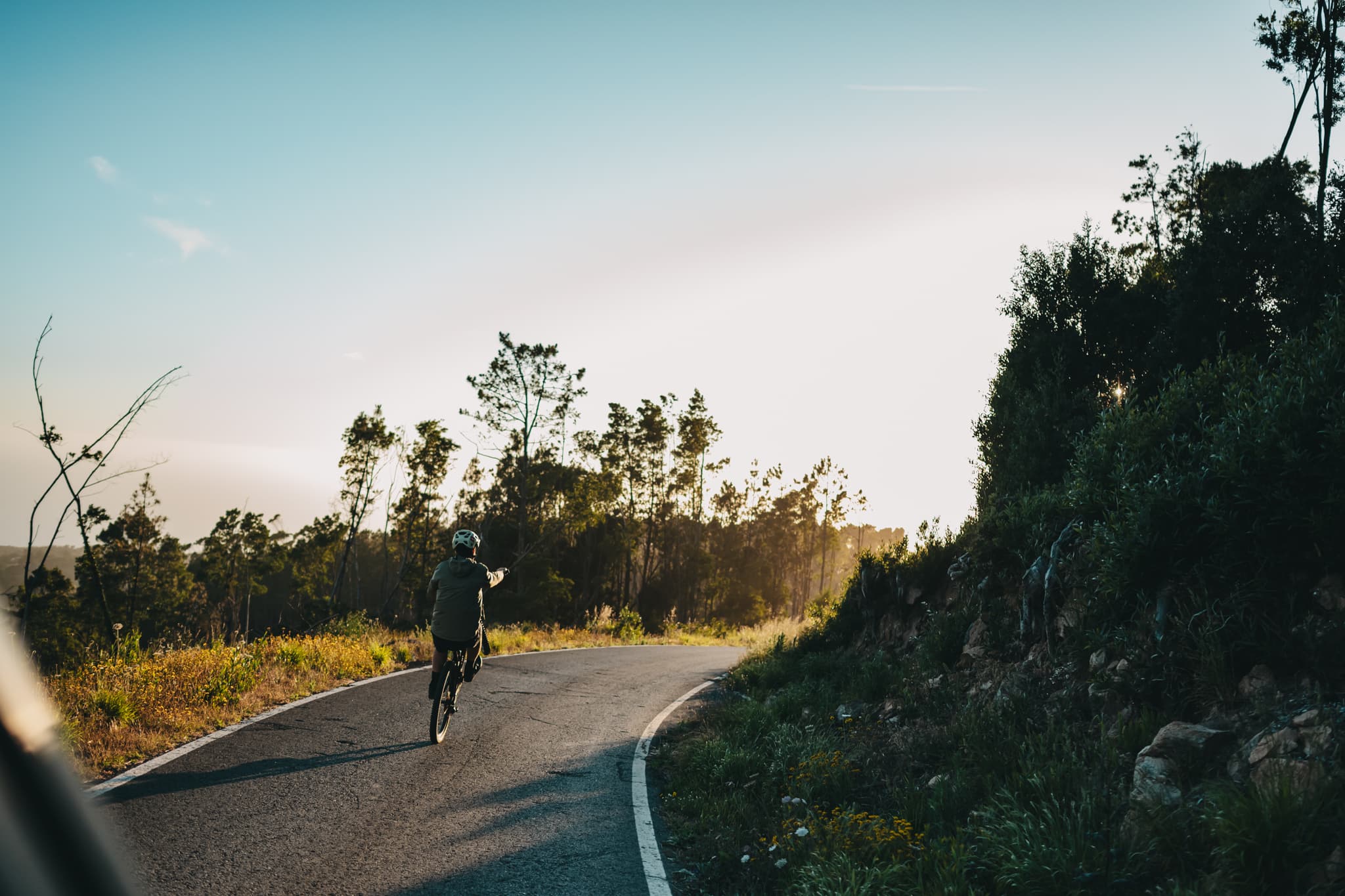 A rider on a quiet gravel road at golden hour, arm raised
